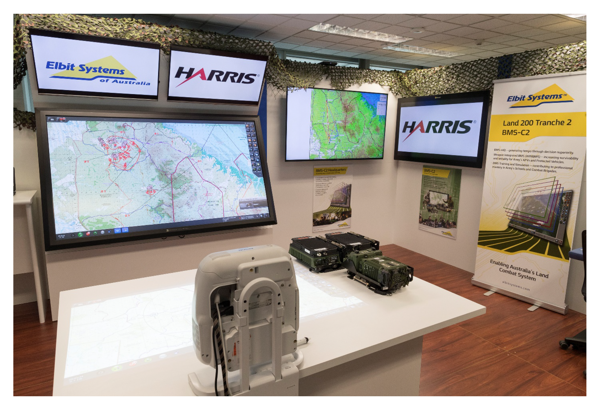 This is a photograph showing the setup of the parts of the Battle Management System. The screens and table illustrate Elbit’s Battle Management System, while the Harris radios provide the Combat Radio System for transmission of Battle Management System da