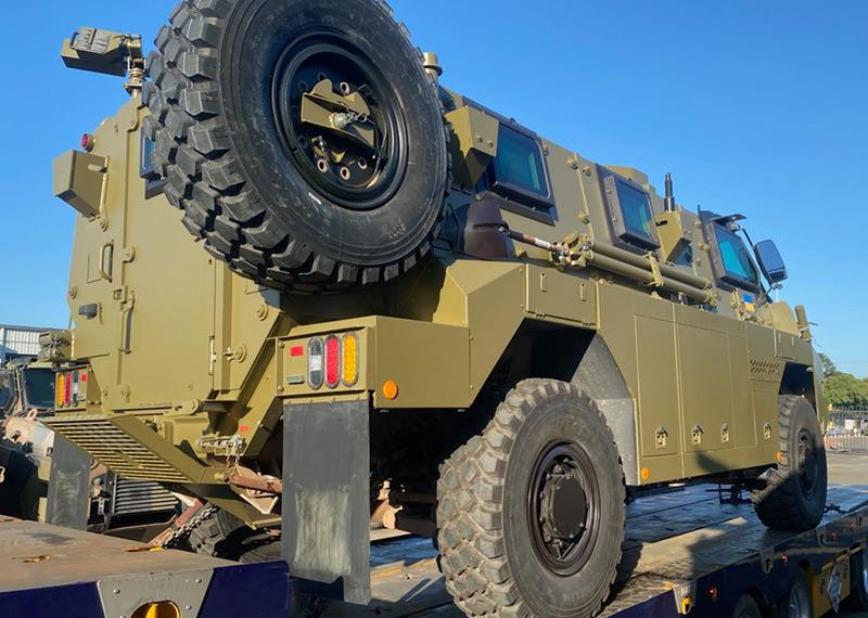 A military vehicle sits on the back of a trailer. 