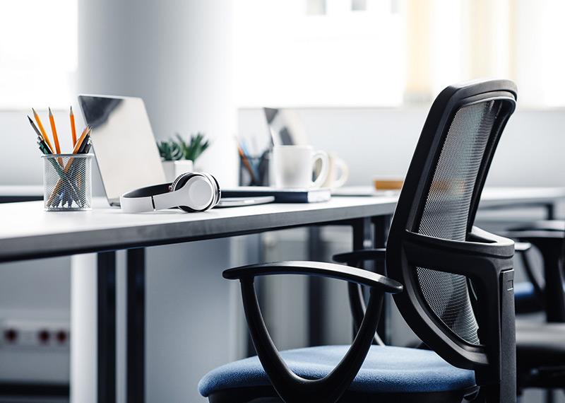 An empty office chair and a desk with a pair of headphones and a laptop. 